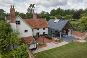 Aerial view of a traditional house with red-tiled roof, a modern extension with metal roofing, patio areas, and landscaped garden.