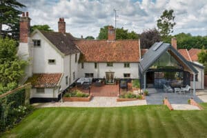 Large traditional house with white walls and red-tiled roof, featuring a modern glass extension and a landscaped backyard with patio and lawn.
