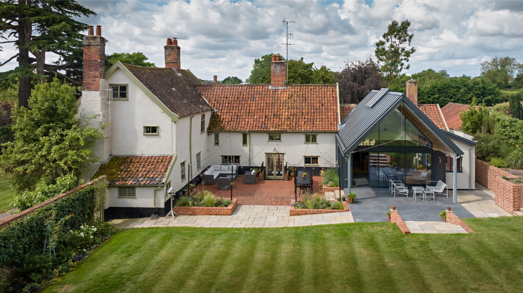 Large traditional house with white walls and red-tiled roof, featuring a modern glass extension and a landscaped backyard with patio and lawn.
