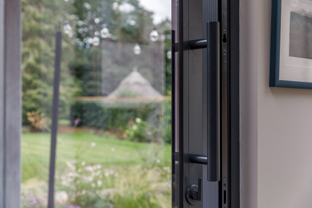 A partially open glass door leads to a garden with green grass, plants, and trees visible outside.