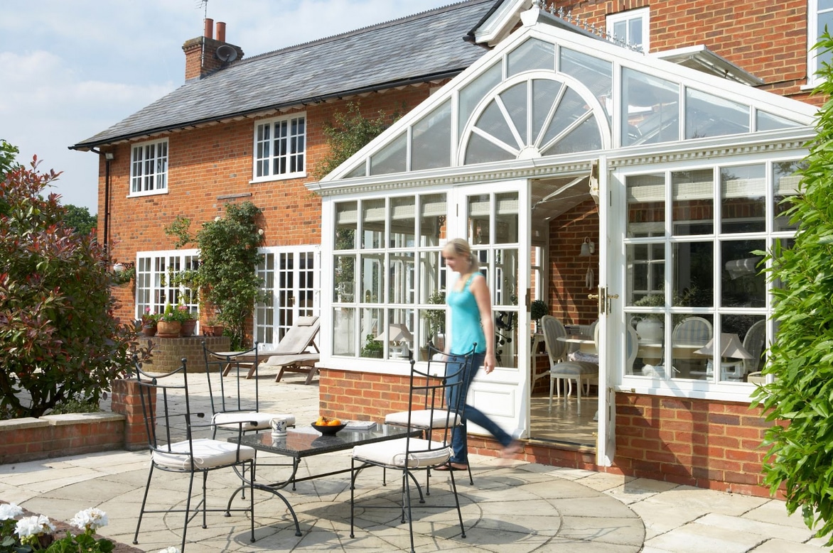 A lady walks out of a traditional timber framed conservatory on to a patio
