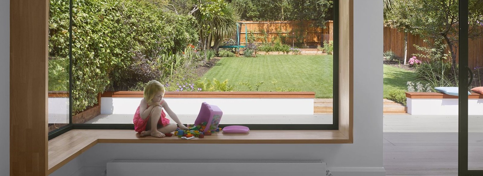 A girl sitting by a frameless glass-to-glass corner window in a modern extension, offering uninterrupted panoramic views.