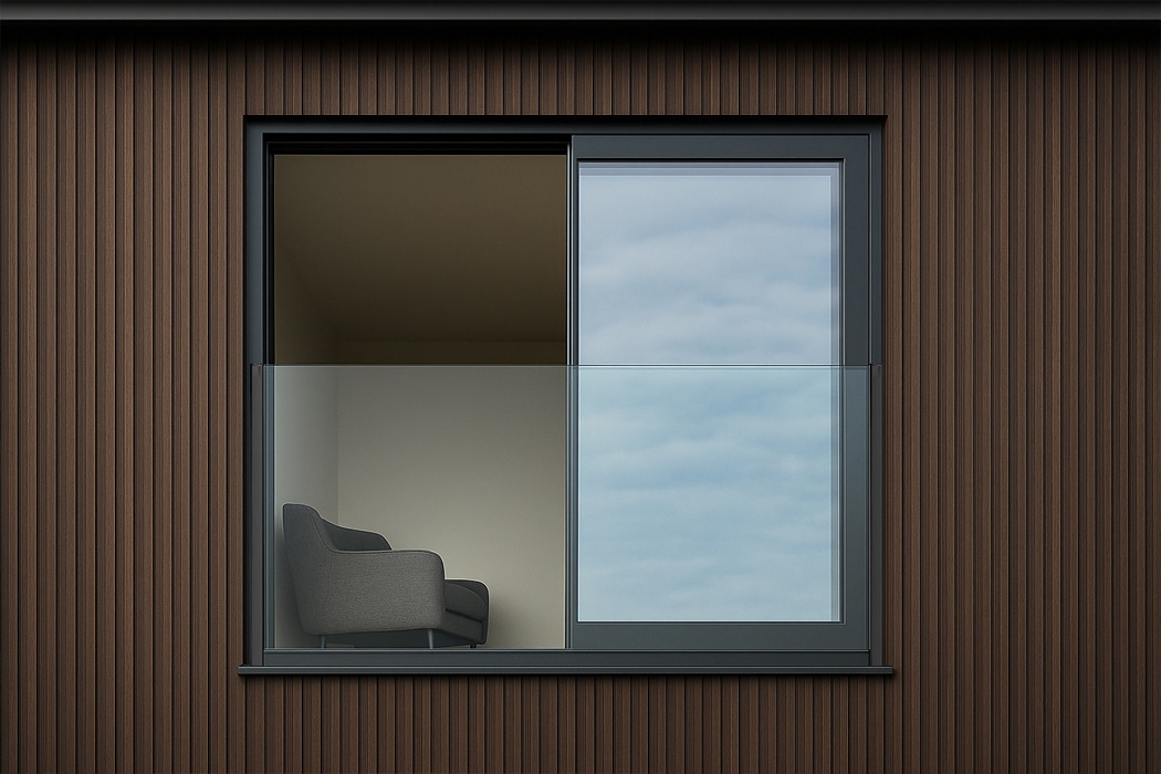 A modern window with a frameless glass balustrade reveals a single gray armchair inside a minimalist room with brown vertical siding on the exterior.