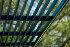 Close-up view of a metal or wooden grid structure with trees and sky blurred in the background.
