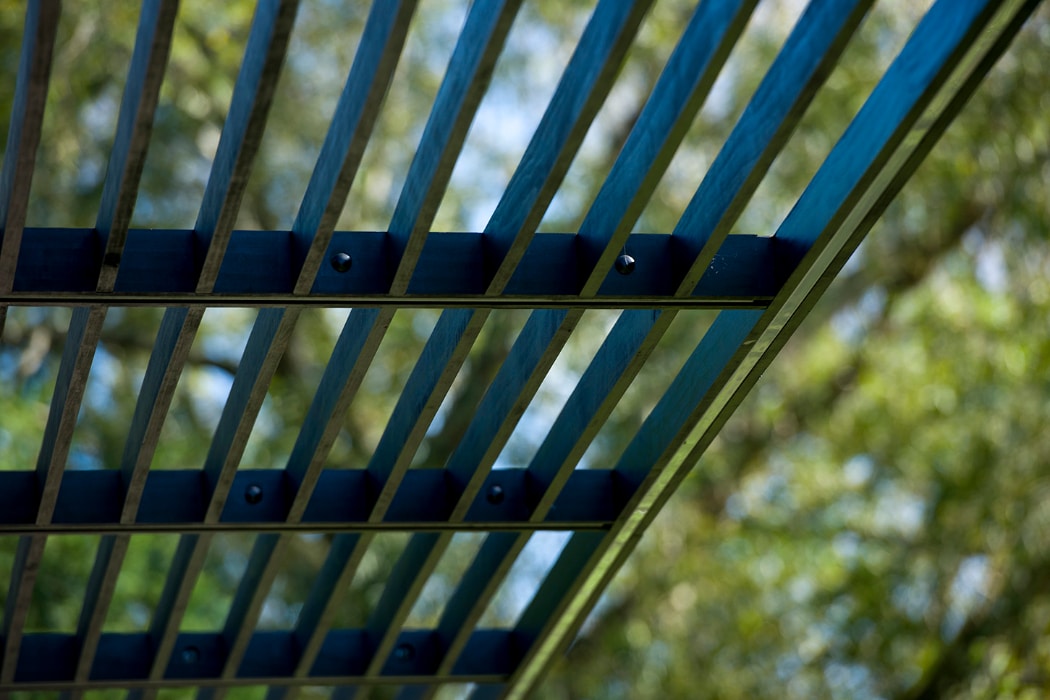 Close-up view of a metal or wooden grid structure with trees and sky blurred in the background.