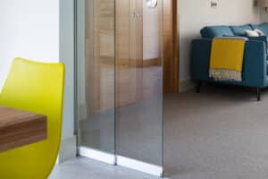 A modern living space featuring a single sliding door, a yellow chair, a wooden table, a blue sofa with a yellow blanket, and beige carpeted flooring.