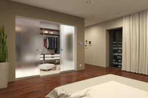 Modern bedroom with a spacious walk-in closet featuring a single sliding frosted glass door, wooden floors, and a potted plant in the corner.