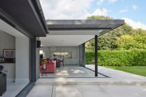 Modern open-plan living space with sliding glass doors leading to a patio and garden, featuring a pink sofa, kitchen, and natural light.