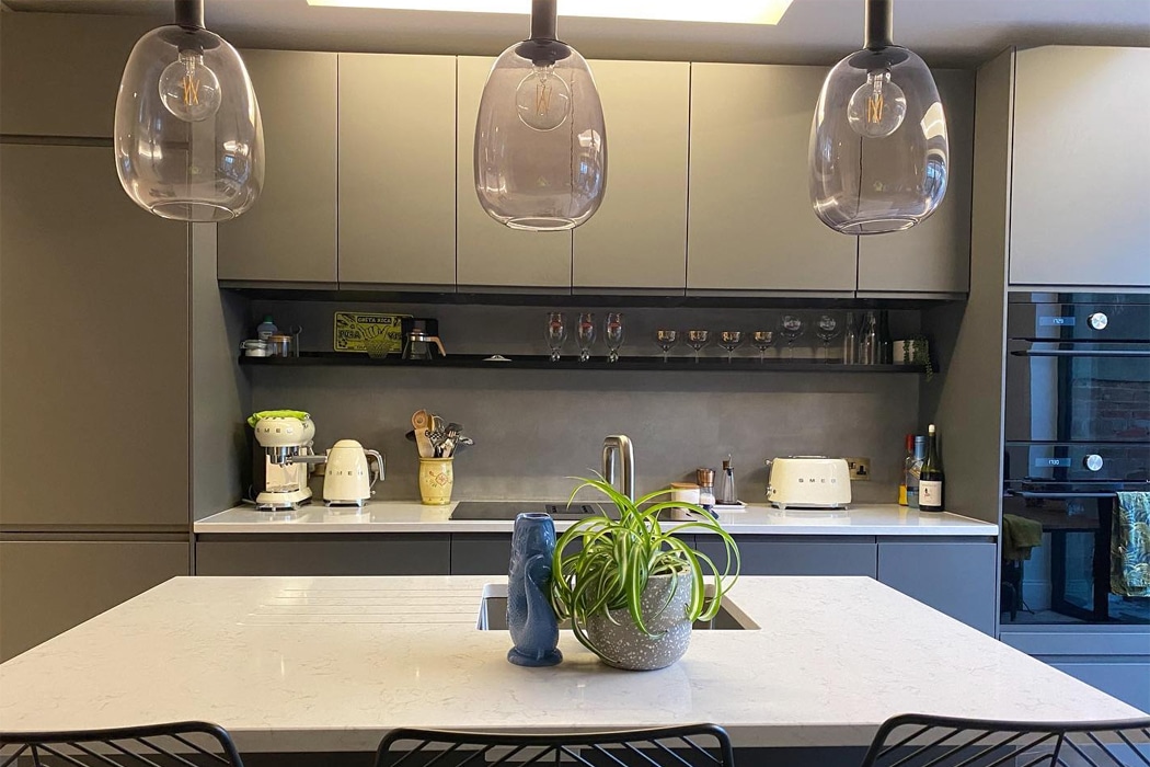 Modern kitchen with gray cabinets, a white countertop island, hanging glass light fixtures, kitchen appliances, and a potted plant on the island.