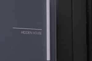 A close-up of a dark gray sign with the words "HIDDEN HOUSE" in white capital letters, mounted next to a black surface.