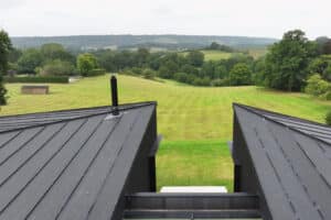 View from a rooftop overlooking a large grassy field with trees and hills in the background under a cloudy sky.