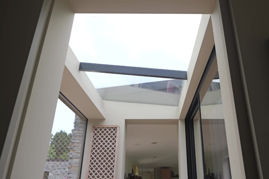 View looking up at a modern building’s glass ceiling with a horizontal beam, large windows, and a lattice panel on the left side.