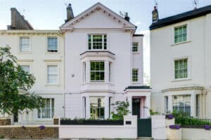 Three-story pale pink townhouse with bay windows and a small front garden, situated between similar light-colored houses on a residential street.