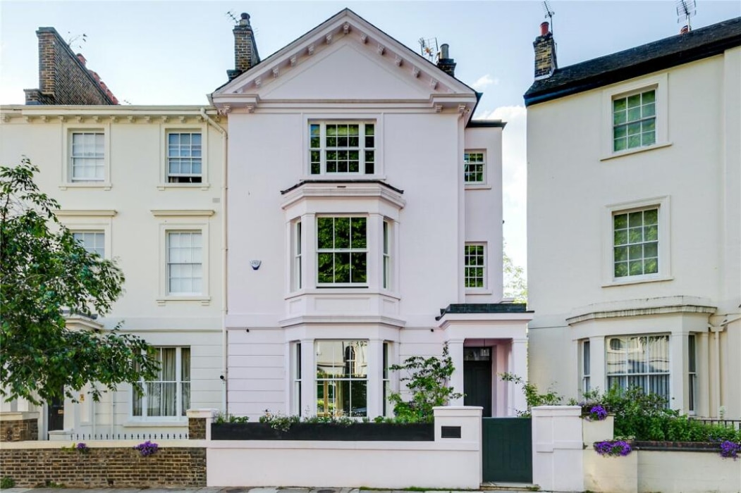 Three-story pale pink townhouse with bay windows and a small front garden, situated between similar light-colored houses on a residential street.
