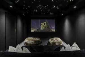 A home theater room with plush seating, two bean bags, a large screen displaying the 20th Century Fox logo, and a ceiling with star-like lights.