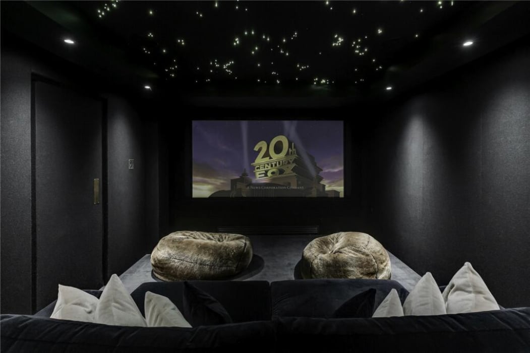 A home theater room with plush seating, two bean bags, a large screen displaying the 20th Century Fox logo, and a ceiling with star-like lights.