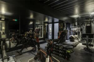 Modern home gym with exercise bikes, treadmill, rowing machine, weight bench, free weights, mirrors, and dark walls, all in a compact, well-lit space.