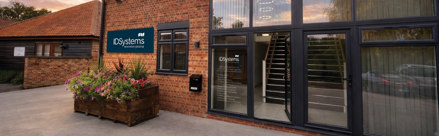 Exterior view of a brick building with large glass entrance doors, a sign reading "IDSystems," and a planter box with flowers near the entrance.