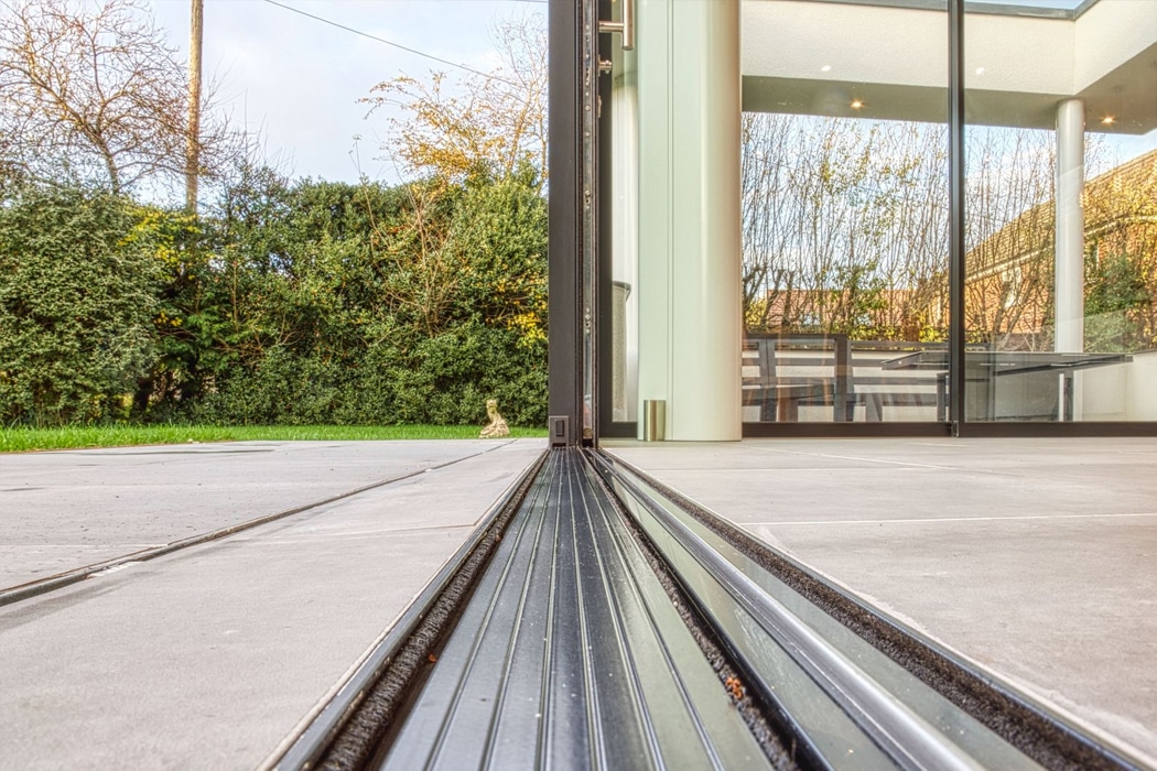 Seamless flush track sliding door threshold viewed from inside modern glass extension overlooking garden landscape.