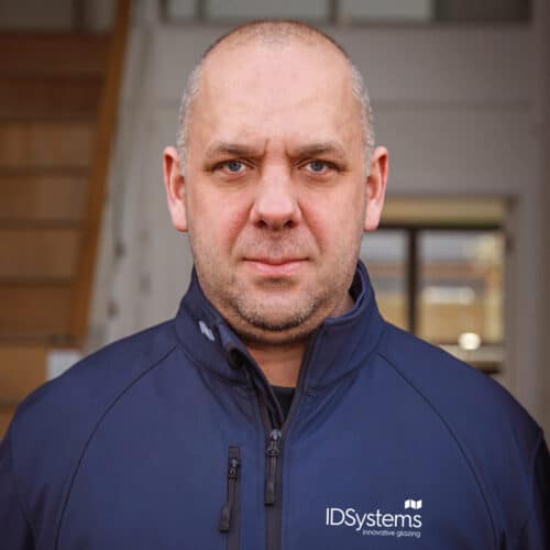 A man stood indoors in front of a staircase, looking directly at the camera.