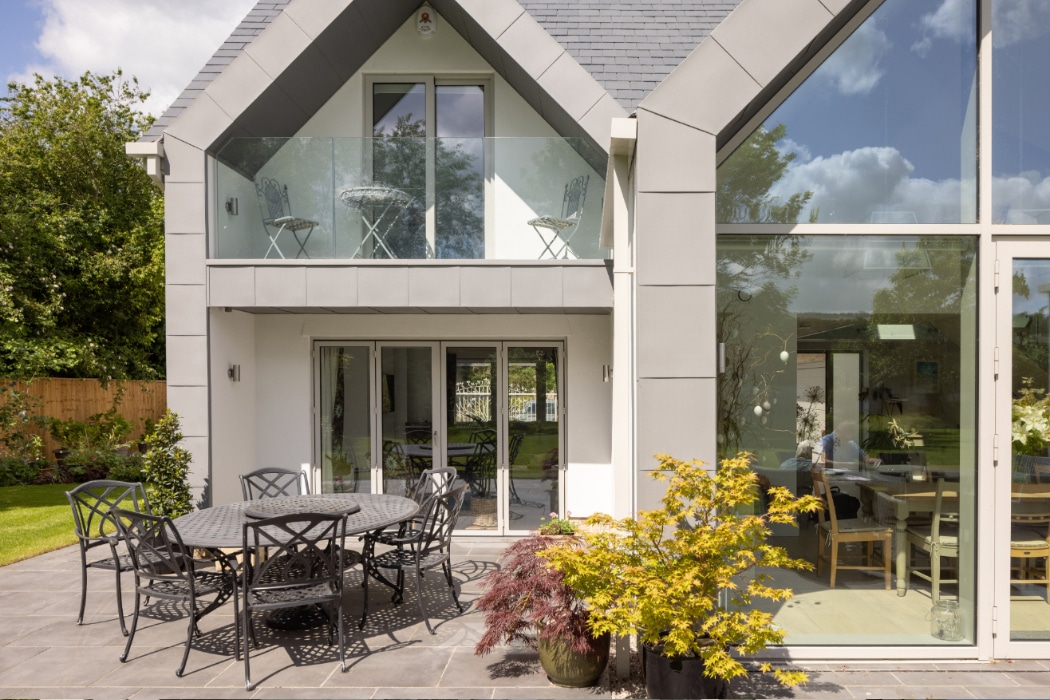 Contemporary white house with aluminium sliding doors and bifold doors opening onto a patio with garden views and outdoor seating.