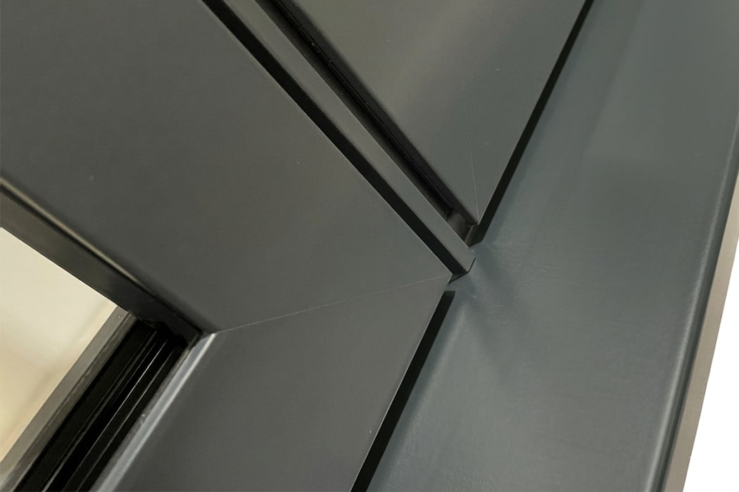 Close-up view of the corner joint of two dark grey metal panels with clean, sharp edges and a smooth finish, reminiscent of the precision seen in aluminium casement windows.