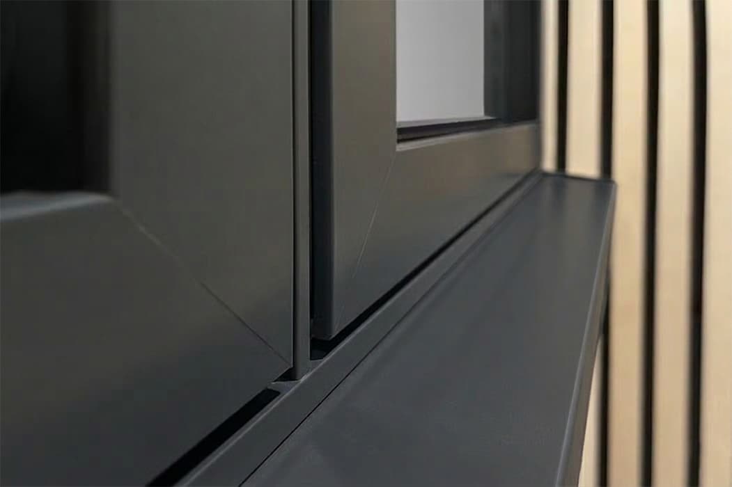 Close-up of a dark grey theVISION aluminium casement window frame with a sleek sill, positioned next to a wall with vertical wooden slats.