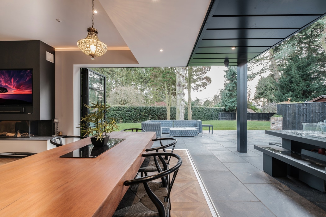 Modern open-plan living space with bifold doors opening to a manicured garden, featuring slim-frame glazing and contemporary interior design.