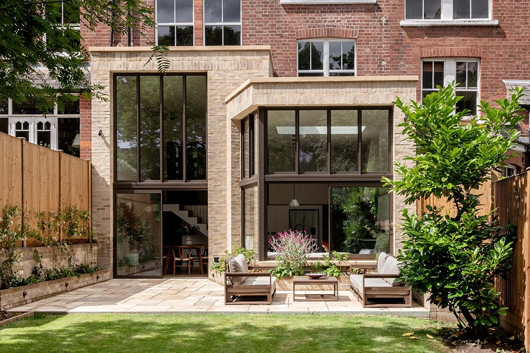 Modern brick extension with double-height glazing and bifold doors opening onto paved terrace and garden.