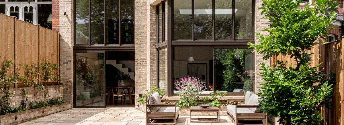 Modern brick Edwardian home with expansive double-height glazing, sliding doors, and contemporary terrace featuring planted boundaries.