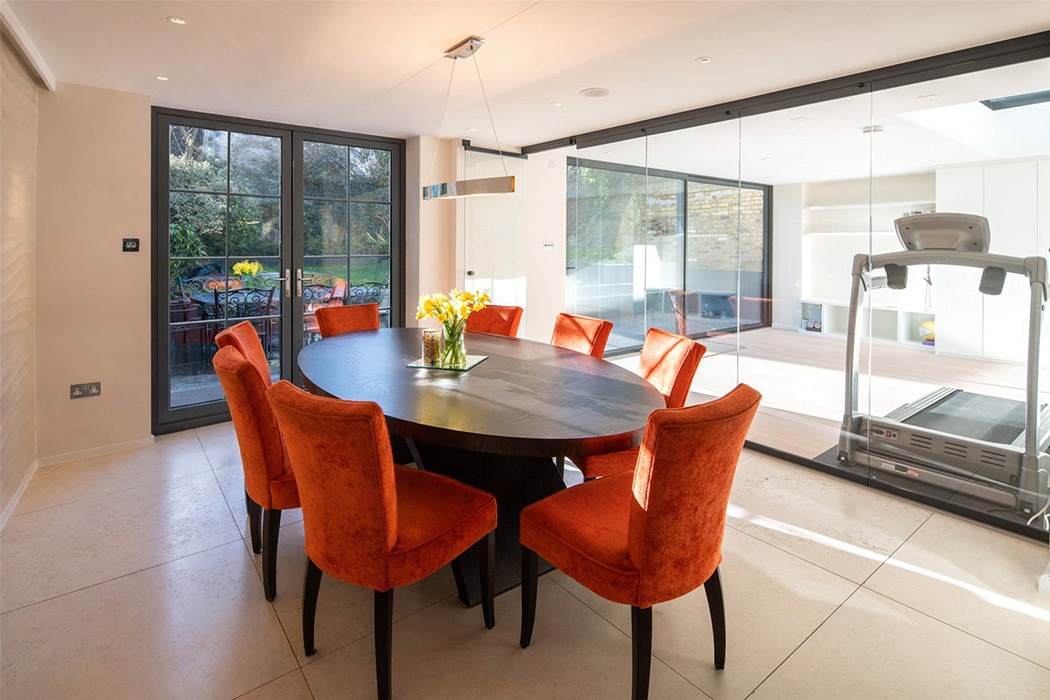 Frameless glass slide and turn door opening to dining space with orange chairs and black table.
