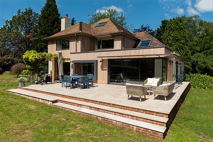 Modern Wiltshire home renovation featuring extensive double-height glazing and bifold doors opening onto a brick-edged patio.