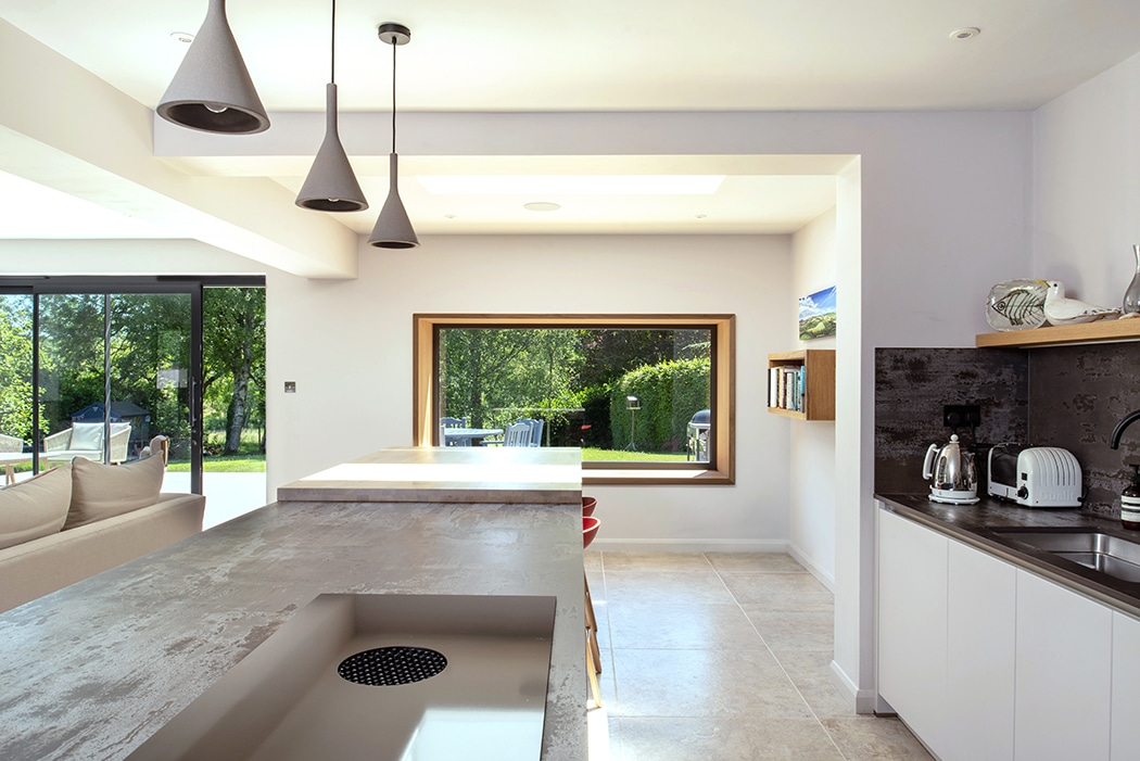 Modern kitchen extension with double-height glazing framing garden views, pendant lights, and integrated appliances.
