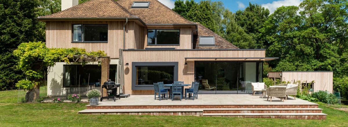 Modern Wiltshire home renovation featuring extensive double-height glazing and sliding doors opening onto a brick terrace and garden.