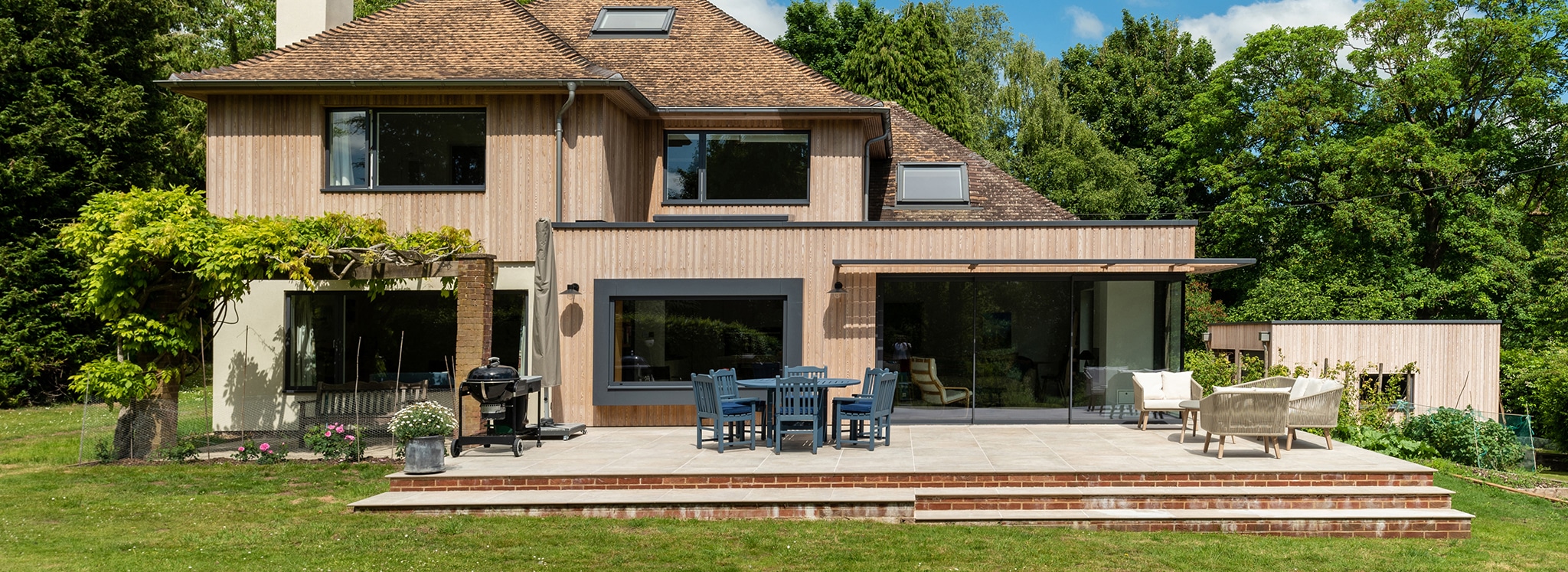 Modern Wiltshire home renovation featuring extensive double-height glazing and sliding doors opening onto a brick terrace and garden.