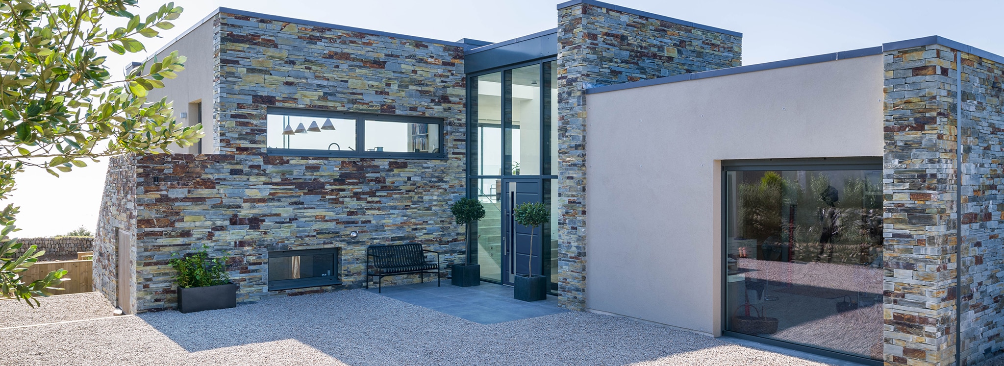 Modern residential home featuring blue-toned slate curtain walling with integrated glazing, creating a contemporary architectural facade with outdoor entertaining space.